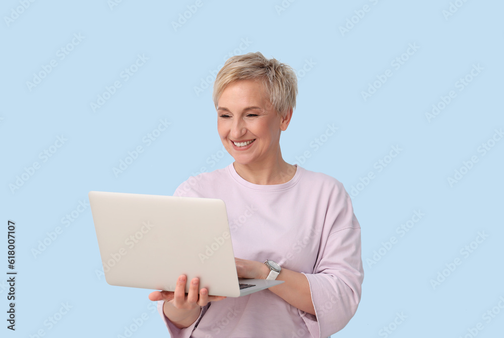 Mature woman using laptop on blue background Mature woman using laptop on blue background