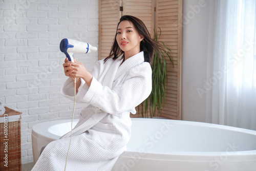 Pretty young Asian woman drying hair in bathroom