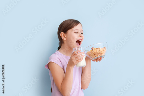 Little girl with milk and cornflakes on light blue background