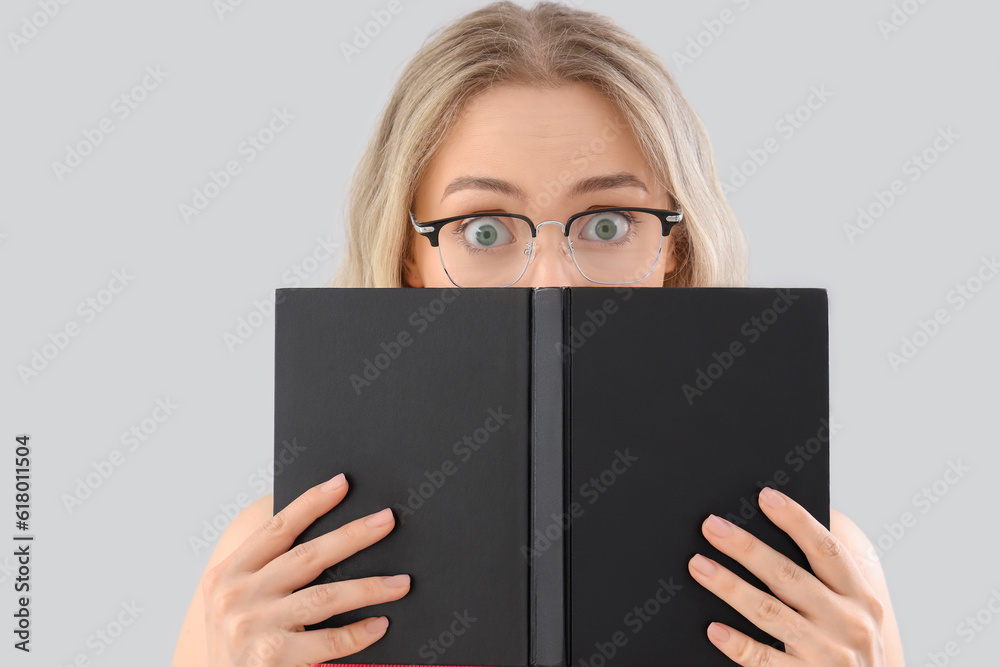 Shocked young woman in stylish eyeglasses reading book on light background, closeup Shocked young woman in stylish eyeglasses reading book on light background, closeup