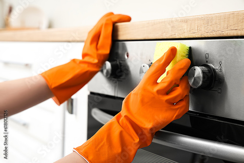 Woman in orange rubber gloves cleaning electric oven with sponge