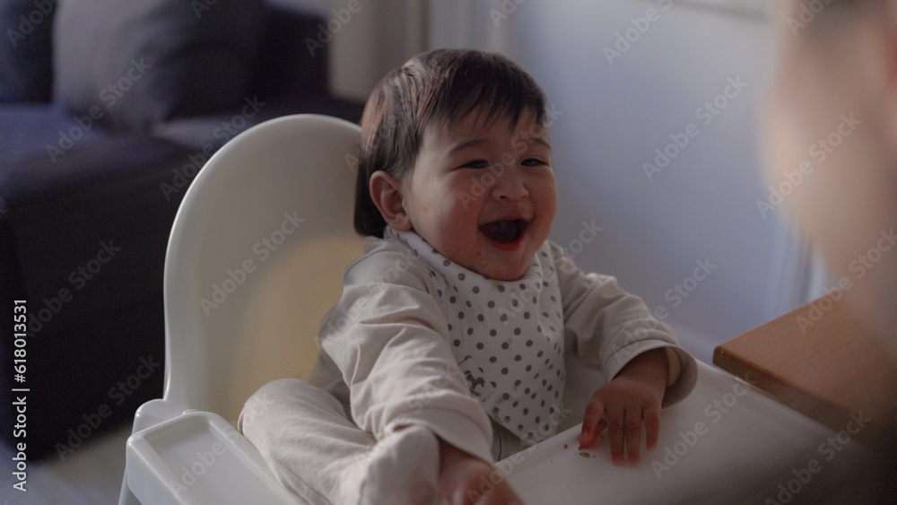 Back view of mom feeding her baby. Toddler is sitting on a high chair and eating with spoon Back view of mom feeding her baby. Toddler is sitting on a high chair and eating with spoon