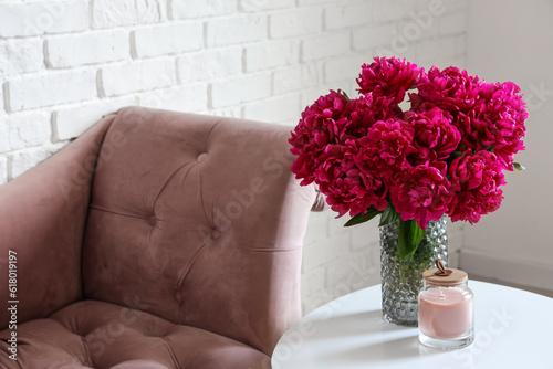 Fototapeta Naklejka Na Ścianę i Meble -  Vase of red peonies with candle on coffee table and couch near white brick wall