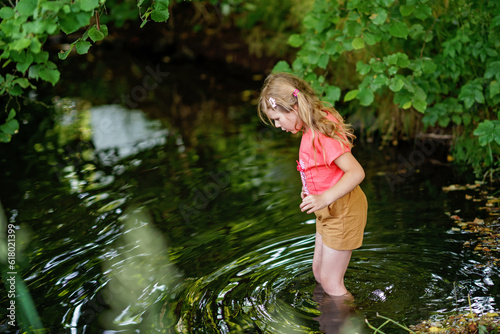 Fototapeta Naklejka Na Ścianę i Meble -  A Happy Girl Embraces the Joys of Childhood as She Explores a Summer Creek, Immersing Herself in Nature's Wonders and Playful Discoveries. Preschool Child and Summertime.