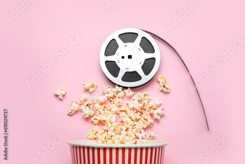 Bucket with tasty popcorn and film reel on pink background