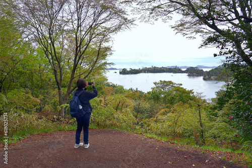 A young female tourist is using a mobile phone to take a picture of the scenery of the bay. Matsushima in Sendai Prefecture, Japan. photo