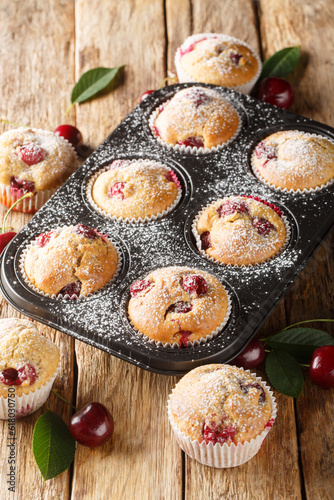 Homemade cherry muffins in cupcake liners and fresh cherries in the background closeup. Vertical
