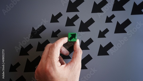 Hand pick wooden block with opposite pointing arrow than others. Unique, different, individuality, stand out from the crowd concept