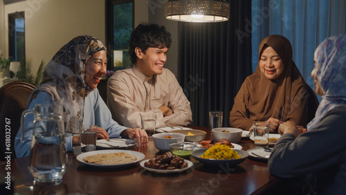 Happy Asia muslim parent and their kids Ramadan dinner together in dining room at home. Family of two generation catering celebration end of Eid al-Fitr togetherness at home. Hari Raya family reunion.