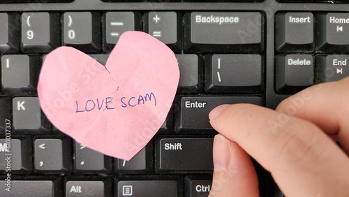 Love scam concept. A crumpled broken hear with the words Love Scam written placed on a keyboard. Victim typing text message to scammer
