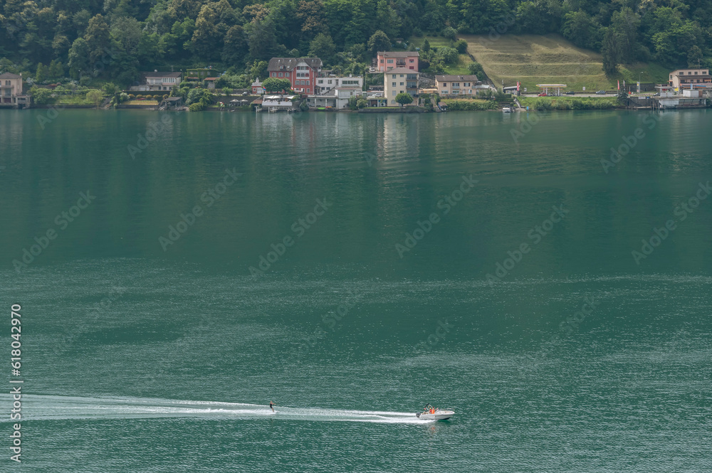 Obraz premium Aerial view of a water ski motorboat on Lake Lugano, with Brusino Arsizio in the background, Switzerland