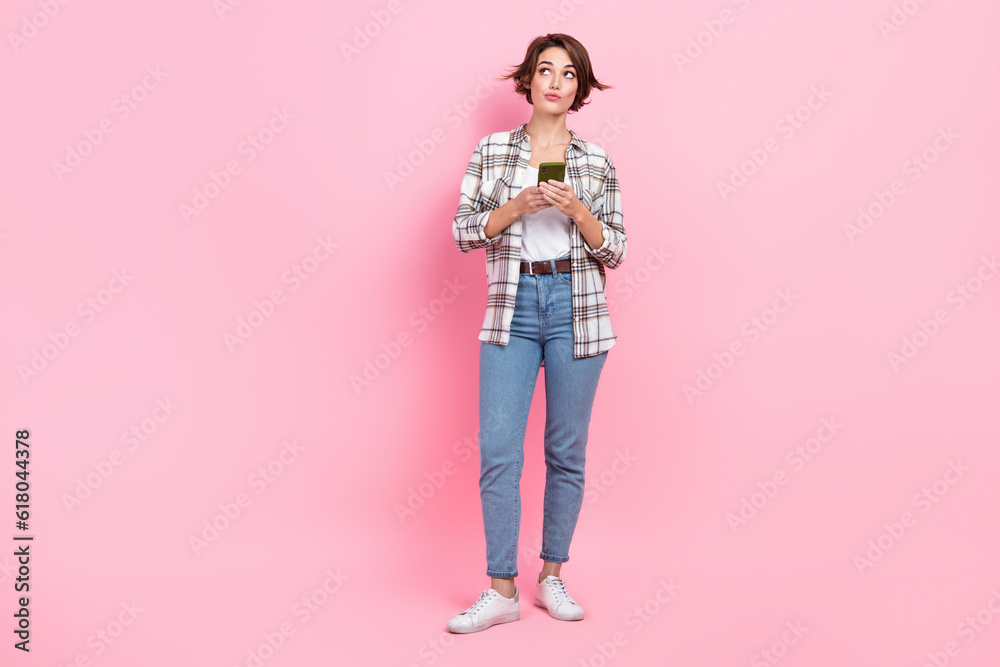Full length photo of minded person hold telephone look empty space brainstorming isolated on pink color background