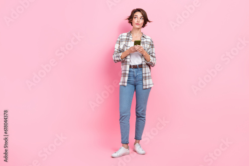 Full length photo of minded person hold telephone look empty space brainstorming isolated on pink color background