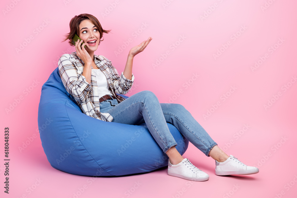 Full length portrait of cheerful person sit cozy bag speak communicate telephone isolated on pink color background