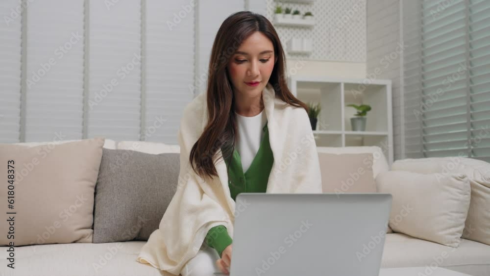Smart working asian female using notebook surfing website and enjoying technology sitting on sofa cover shoulder by blanket in living room at home. Freelance occupation and holiday activity concept. Smart working asian female using notebook surfing website and enjoying technology sitting on sofa cover shoulder by blanket in living room at home. Freelance occupation and holiday activity concept.