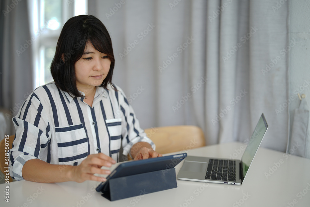 A woman is using a digital tablet and working on a laptop on the white table. A woman is using a digital tablet and working on a laptop on the white table.