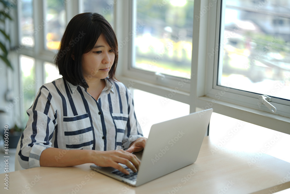 An Asian woman is working on a laptop seriously for business jobs in a cozy room. An Asian woman is working on a laptop seriously for business jobs in a cozy room.