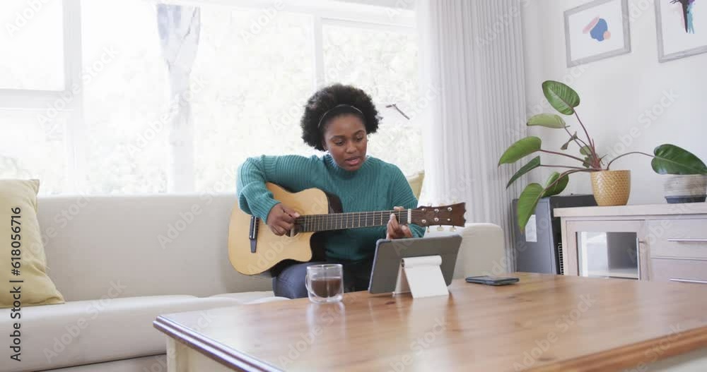 Happy african american woman practicing playing guitar using tablet at home, slow motion Happy african american woman practicing playing guitar using tablet at home, slow motion