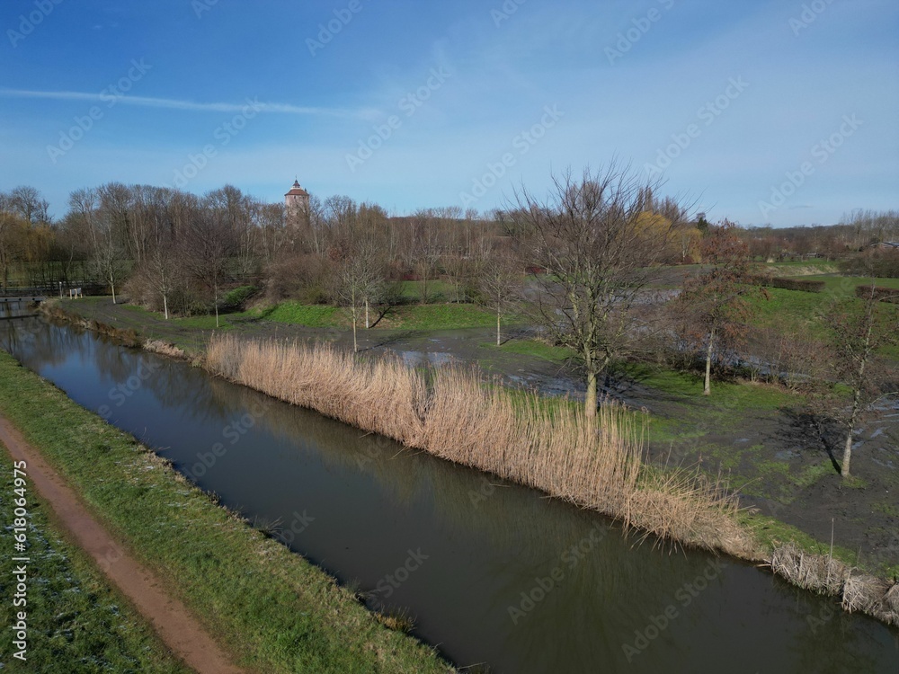 a long narrow waterway surrounded by grass, trees, and a dirt road a long narrow waterway surrounded by grass, trees, and a dirt road