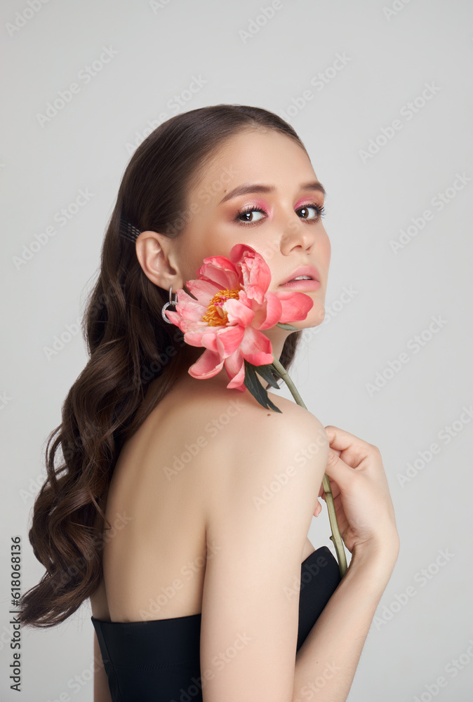 Beauty Woman with big pink flowers, studio portrait. Perfect body, pink professional makeup on a woman face. Curly hair Beauty Woman with big pink flowers, studio portrait. Perfect body, pink professional makeup on a woman face. Curly hair