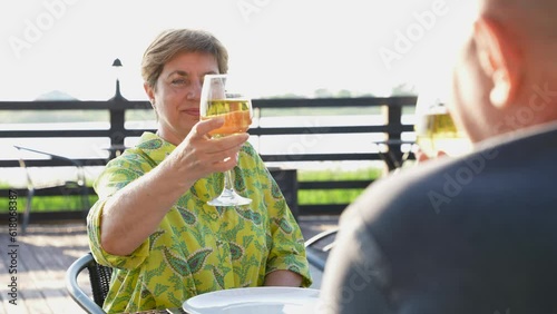 Senior man and senior woman having dinner outside, celebrating with glasses of wine or drink. Eating and having fun together on weekend. Summertime on the veranda. Slow motion