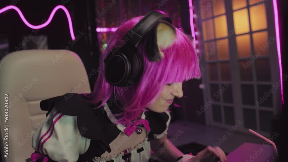 Portrait of gen Z girl wearing cosplay outfit with pink wig, neko ears and headset playing video game on desktop computer