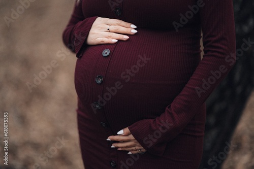 Closeup of pregnant woman in burgundy dress touching her belly