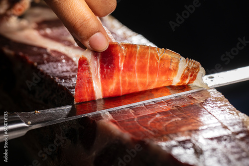 Jamón ibérico bellota Acorn-fed Iberian ham. Iberian ham cutter with knife making the best slice for tasting.  Jamón Ibérico ham cut with knife with selective focus and black background for copy space