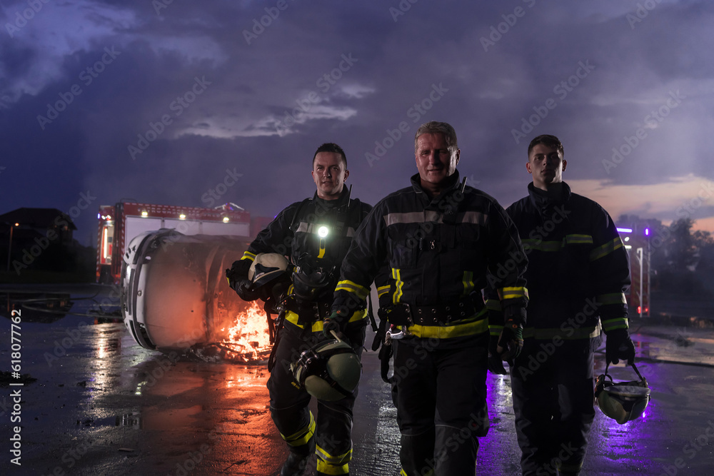 Brave Firefighters Team Walking to the Camera. In Background Paramedics and Firemen Rescue Team Fight Fire in Car Accident, Insurance and Save Peoples Lives concept. Brave Firefighters Team Walking to the Camera. In Background Paramedics and Firemen Rescue Team Fight Fire in Car Accident, Insurance and Save Peoples Lives concept.