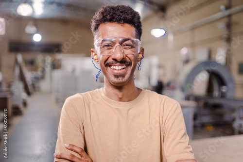 retrato de um homem afro Brasileiro professor de curso técnico de braços cruzados sorrindo para a câmera e usando óculo de proteção em um ambiente industrial photo