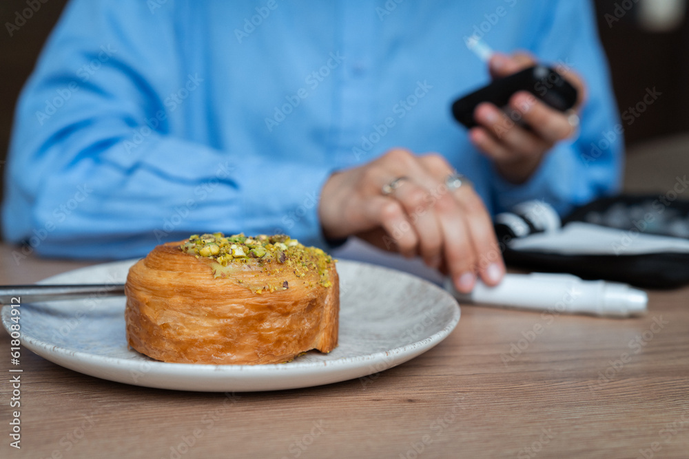 Croissant with pistachio grain and woman measuring blood sugar on background
