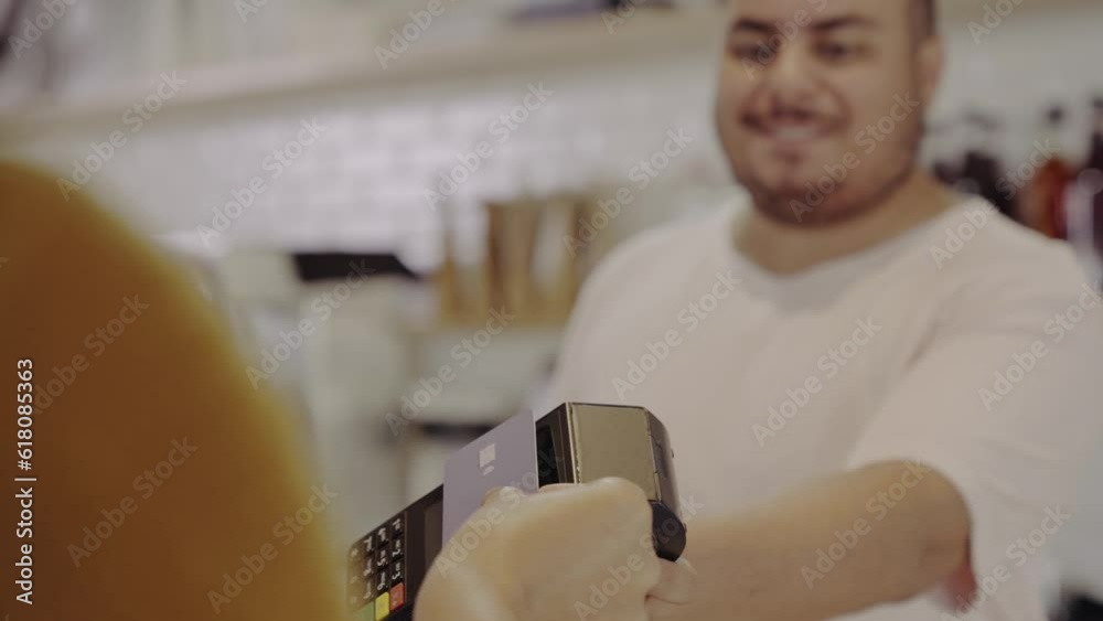 atendente Brasileiro recebendo o pagamento de uma cliente com cartao de credito por aproximacao em uma cafeteria no Brasil