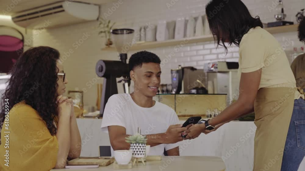 jovem latino usando o celular para fazer pagamento por aproximacao em uma cafeteria no Brasil