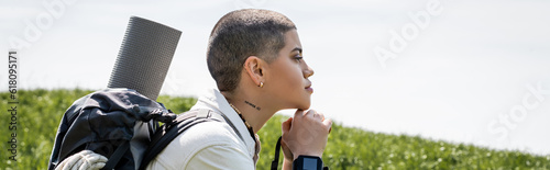 Slika na platnu Side view of young short haired and tattooed female hiker with backpack and fitn