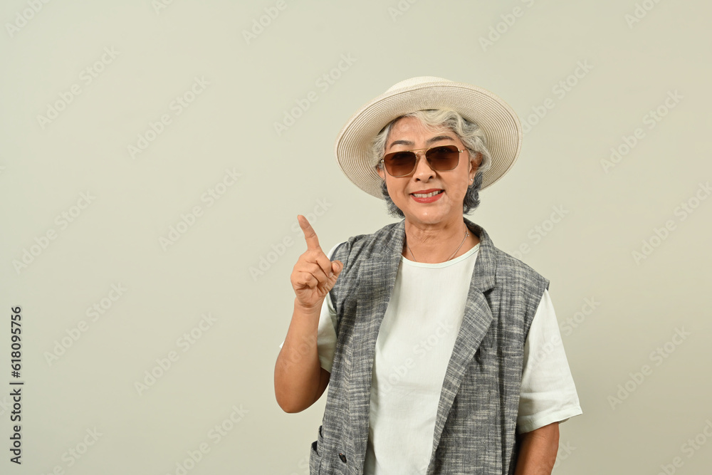 Smiling retired woman in sunglasses and hat, pointing aside, shows space for your advertisement or promotional text Smiling retired woman in sunglasses and hat, pointing aside, shows space for your advertisement or promotional text
