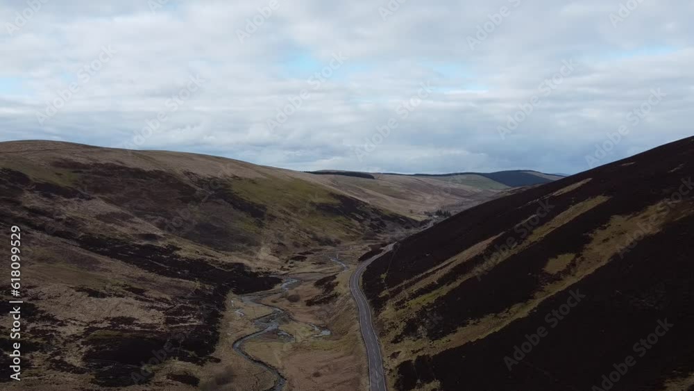 Drone view of a driving road and a river between dry hills on a cloudy sky Drone view of a driving road and a river between dry hills on a cloudy sky
