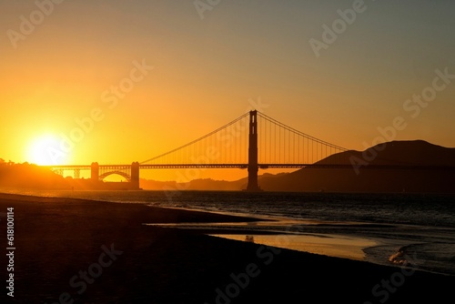 Stunning shot of a sun-drenched bridge and bay  with a brilliant orange sky in the background
