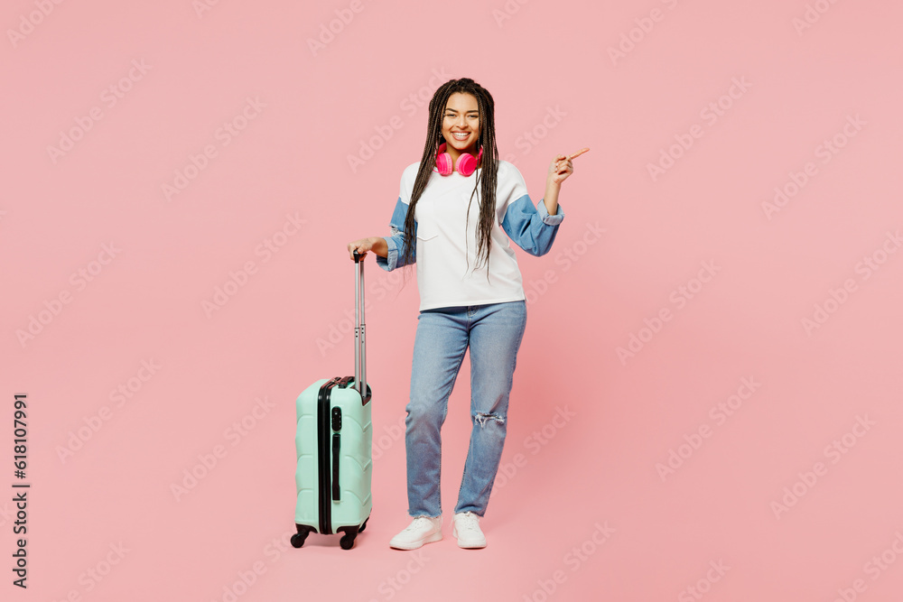 Traveler woman wear casual clothes hold suitcase bag point finger aside isolated on plain pastel pink background. Tourist travel abroad in free spare time rest getaway Air flight trip journey concept