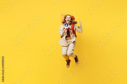 Full body young woman carry bag with stuff mat jump high scream in megaphone isolated on plain yellow background Tourist leads active lifestyle walk on spare time Hiking trek rest travel trip concept #618108503