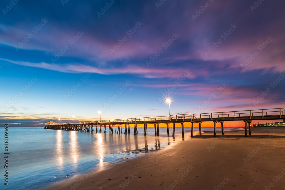 Henley Beach jetty at dusk with the tranquil sea embracing the weathered pillars with purple cluds above, South Australia