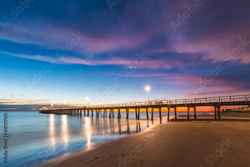 Henley Beach jetty at dusk with the tranquil sea embracing the weathered pillars with purple cluds above, South Australia