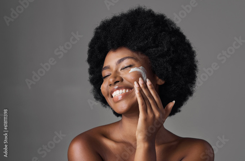 Beauty, skin care and black woman with lotion on face, afro and cosmetics in studio on grey background. Natural skincare, collagen cream and African model with salon glow, dermatology and wellness.