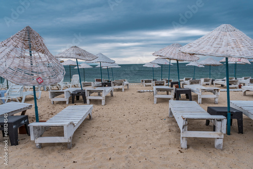 Sun bed chairs with matress and straw beach umbrellas on beach. Blue hour time background by the sea.. © Birol