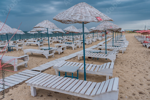 Sun bed chairs with matress and straw beach umbrellas on beach. Blue hour time background by the sea.. © Birol
