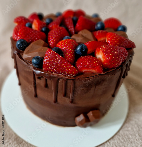 cheesecake with chocolate frosting and fruit around the perimeter. sprinkle with cocoa powder. raspberries and strawberries blueberries. cylinder shape ready to celebrate on a tray, flower, 