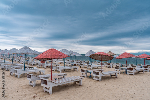 Sun bed chairs with matress and straw beach umbrellas on beach. Blue hour time background by the sea..