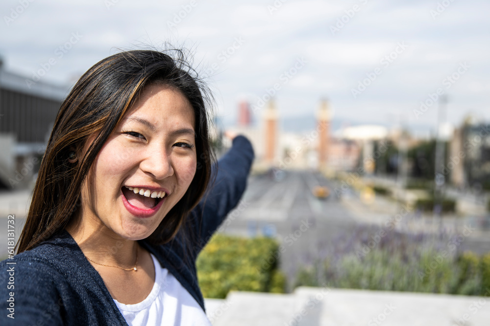Happy handsome woman smiling relaxed and looking at camera in the street taking a selfie. Relaxed happy lady laughing and staring and holding the camera standing outdoors with a city landscape behind.
