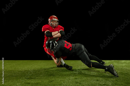 Competitive spirit. Two men, american football players in full uniform and equipment on field playing over black background. Professional sport, action, lifestyle, match, hobby, training, ad concept