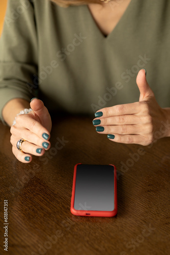 The hands of a woman are gesticulating. There is a smartphone on the table