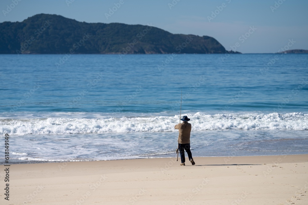 man fishing on the beach at dusk in queensland australia. casting a fishing line in from the beach